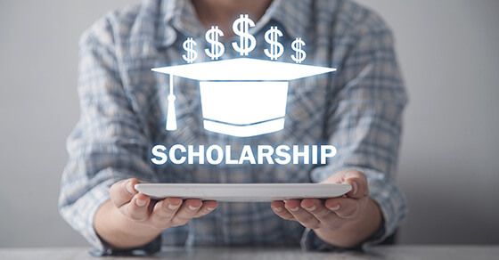 Woman holding a paper with an image of a graduation cap and the word Scholarship over it