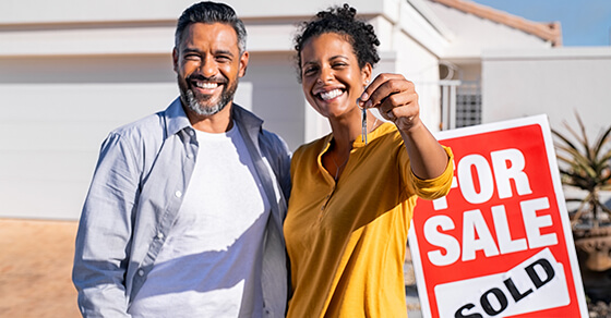 Couple holding a house key in front of a home with a sold sign