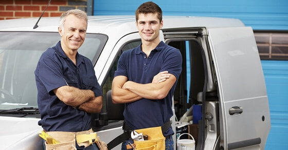 Father and son standing in front of a van wearing tool belts
