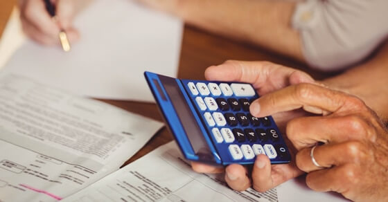 Close up of male's hands holding a calculator with bills underneath his hands