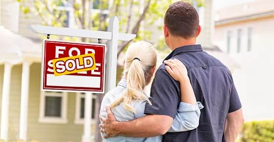Couple hugging looking at a home with a sold sign in front of it