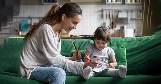 Mother helping her toddler daughter color while sitting on a green couch