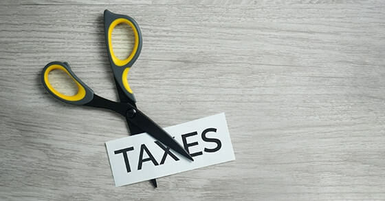 Pair of scissors cutiing a piece of paper in half with the word "Taxes" on it